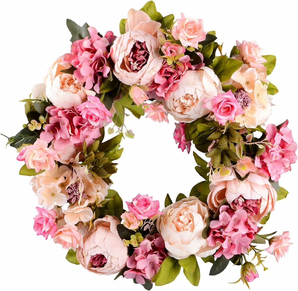 Pink artificial peony flower wreath with greenery on grapevine base hanging on front door