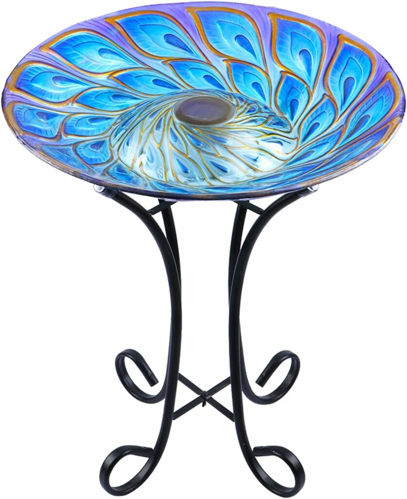 Solar glass peacock bird bath with LED lights on foldable metal stand in garden at dusk